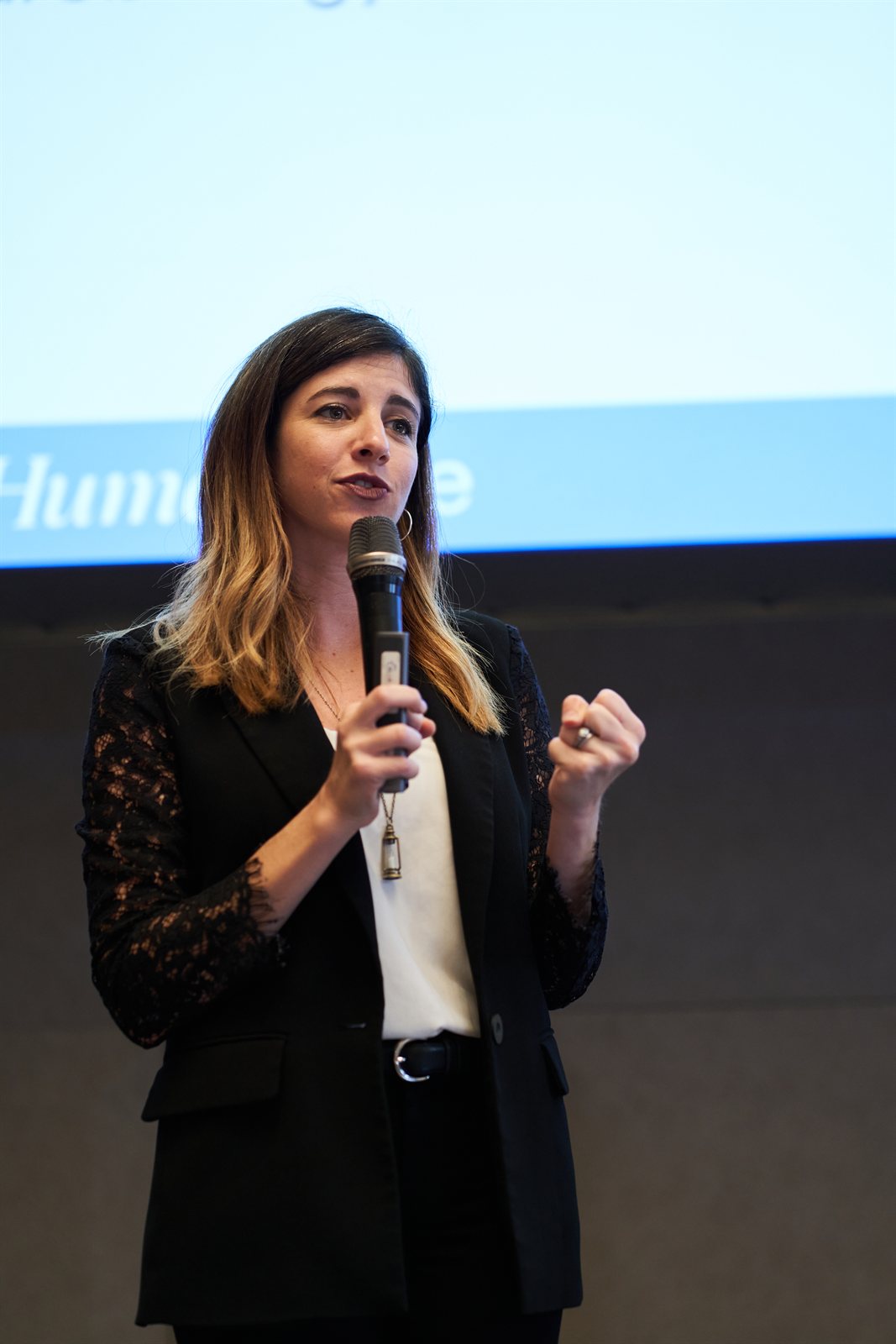 A HumanSide facilitator presenting with a microphone, HumanSide screen behind her